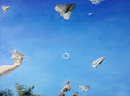 Paper airplanes being thrown into the air against a blue sky with a person's hands visible.