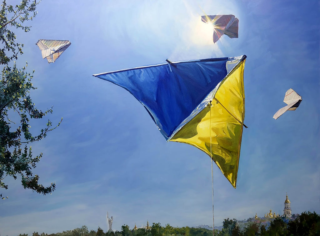 Colorful kites flying against a blue sky with trees and a building in the background.
