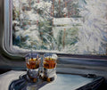 Two shot glasses with a dark liquid on a surface near a window with a snowy landscape.