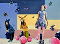 Colorful artwork of four people in costumes with a stylized background featuring butterflies and balls.