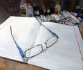 Eyeglasses on an open notebook with art supplies in the background