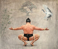 Man in traditional attire performing a yoga pose with a crane and bamboo in the background