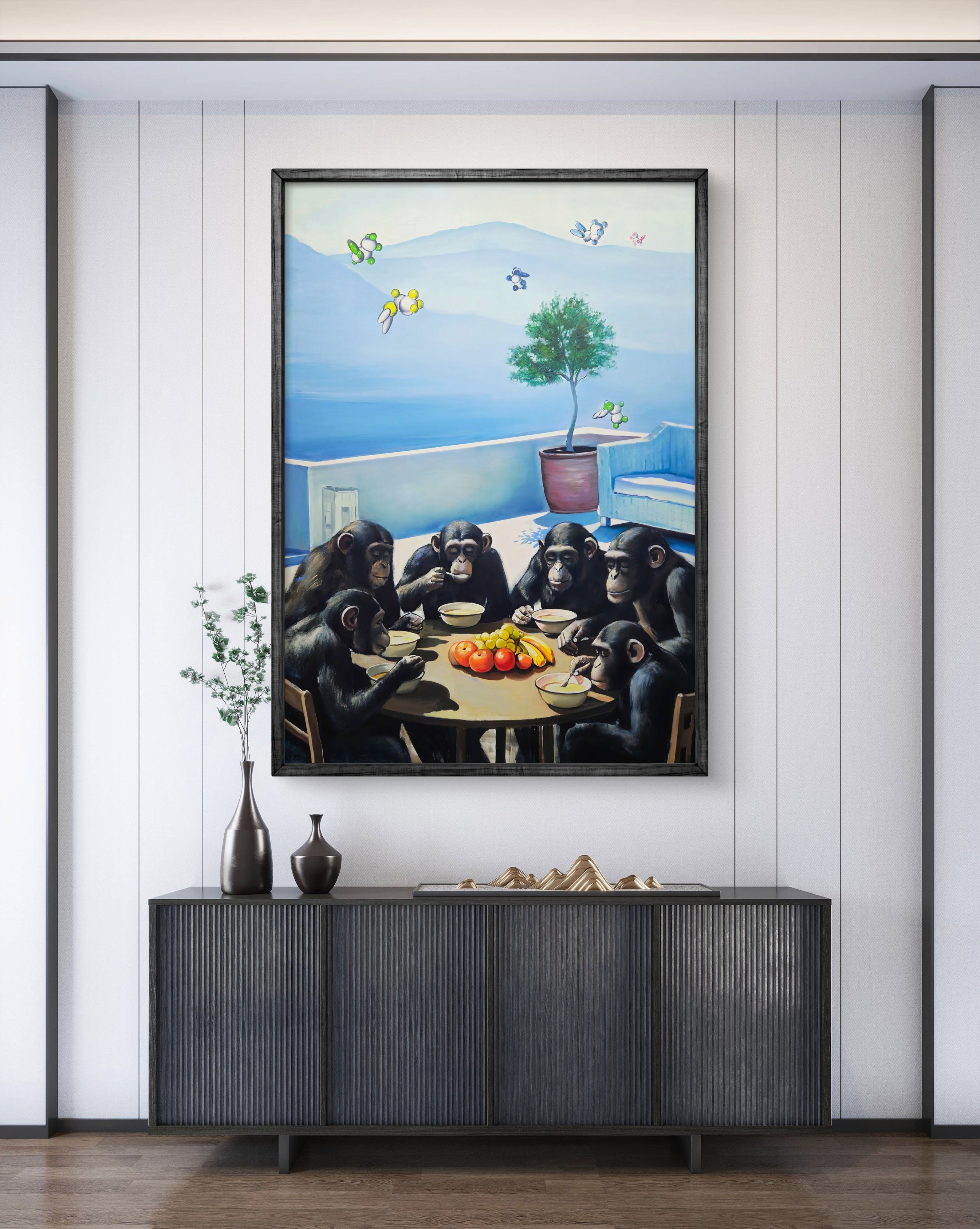 Framed artwork of chimpanzees around a table with fruit, mounted on a wall above a dark piece of furniture.