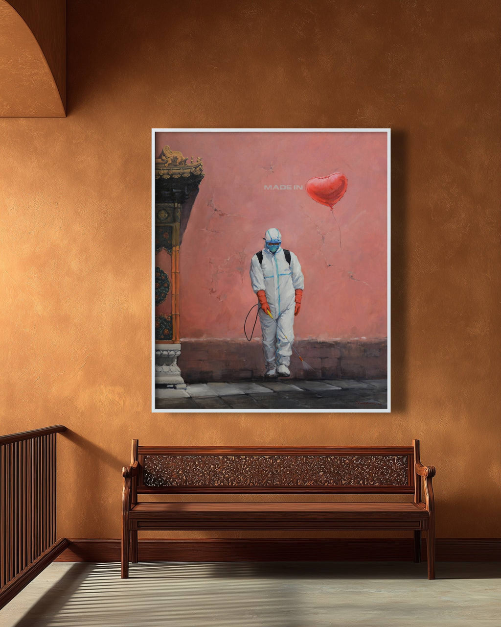 Framed artwork of a person in protective gear with a red heart balloon on a brown wall above a wooden bench.