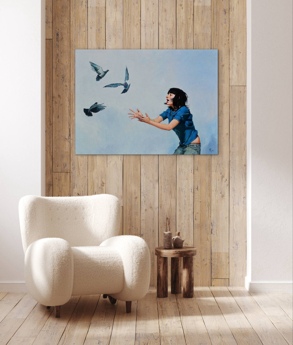 Room interior with a white armchair, wooden side table, and a painting of a woman with birds on the wall.