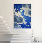 Framed artwork of a person on a cloud against a blue sky with clouds, displayed on a white wall.