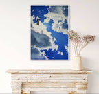 Framed artwork of a person in the sky above a wooden console table with a vase of dried flowers.