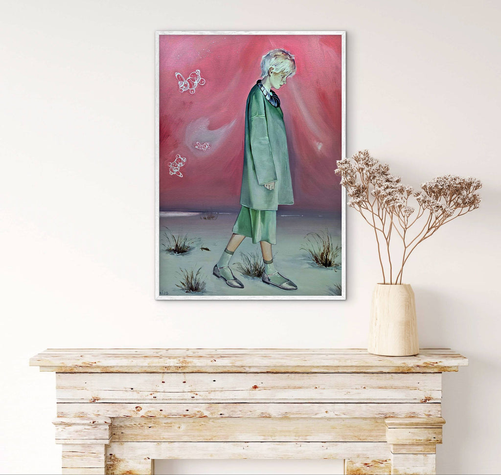 Framed artwork of a person in a green outfit against a pink sky, displayed on a white wall above a wooden console table.