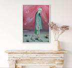 Framed artwork of a person in a green outfit against a pink sky, displayed on a white wall above a wooden console table.