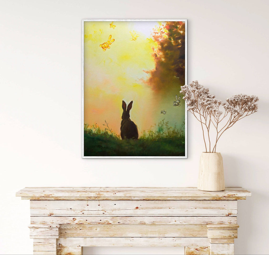 Framed artwork of a rabbit in a field with a butterfly, placed on a wooden surface.