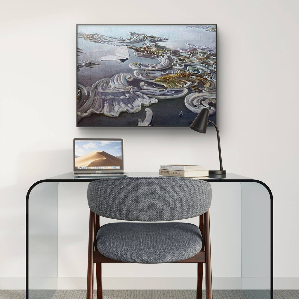 Modern office setup with a glass desk, gray chair, laptop, and framed artwork on a white wall.