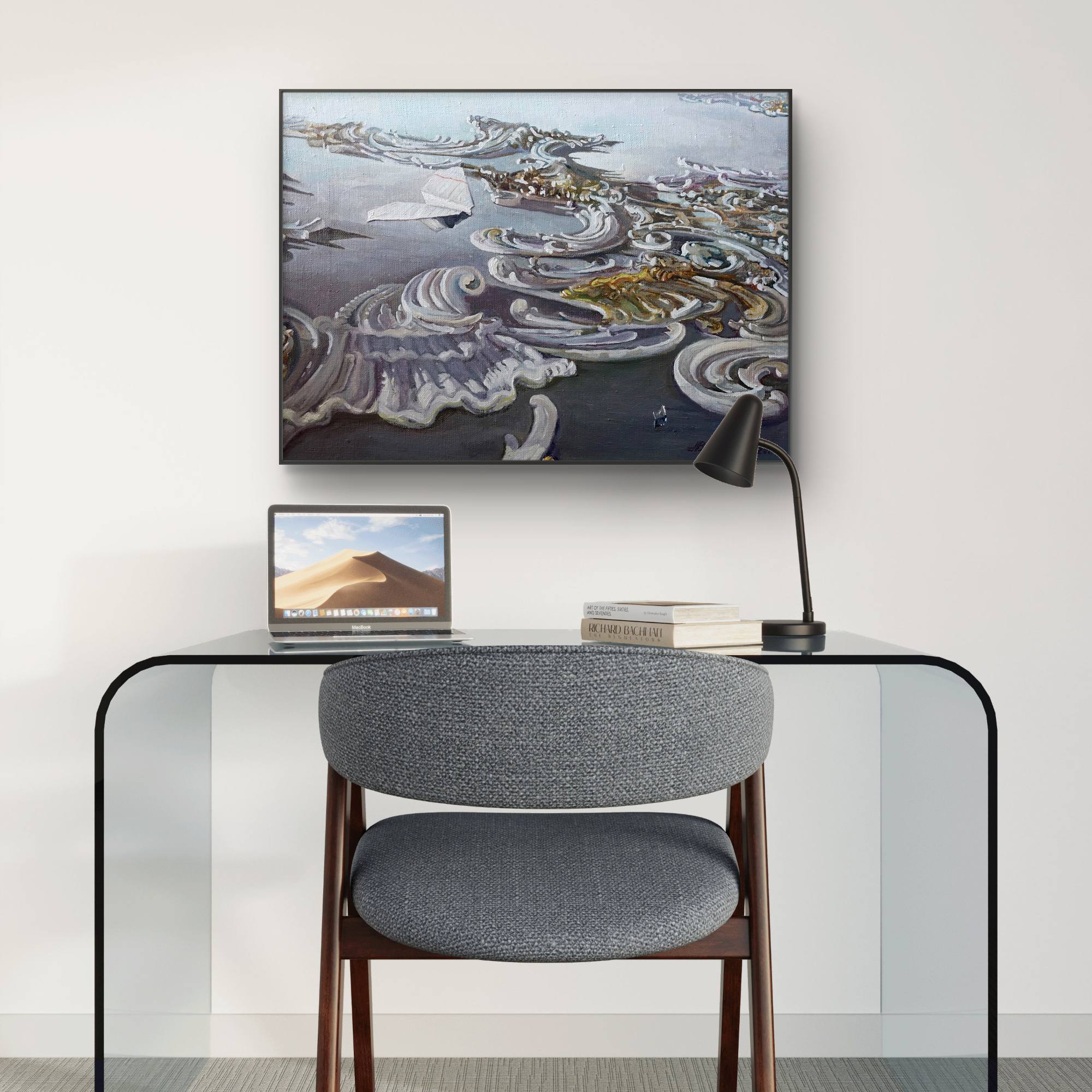 Modern office setup with a glass desk, gray chair, laptop, and framed artwork on a white wall.