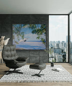 Modern living room with a gray armchair, ottoman, and a large painting of a beach scene.
