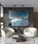 Modern living room with two white armchairs and a large abstract painting on a marble wall.