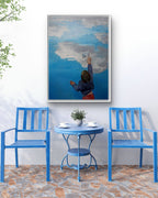 Blue chairs and table set against a white wall with a large framed picture of a child painting a cloud.