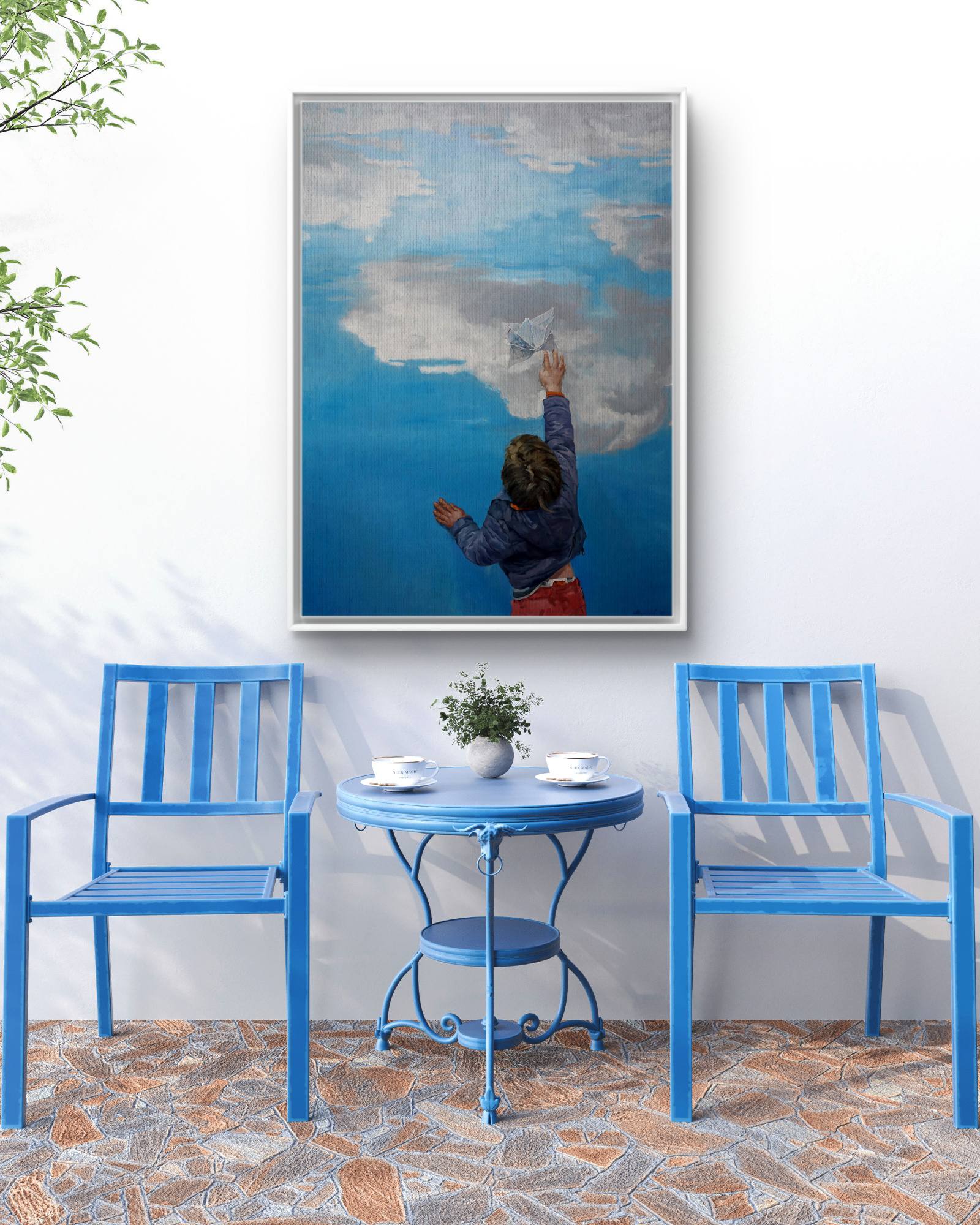 Blue chairs and table set against a white wall with a large framed picture of a child painting a cloud.