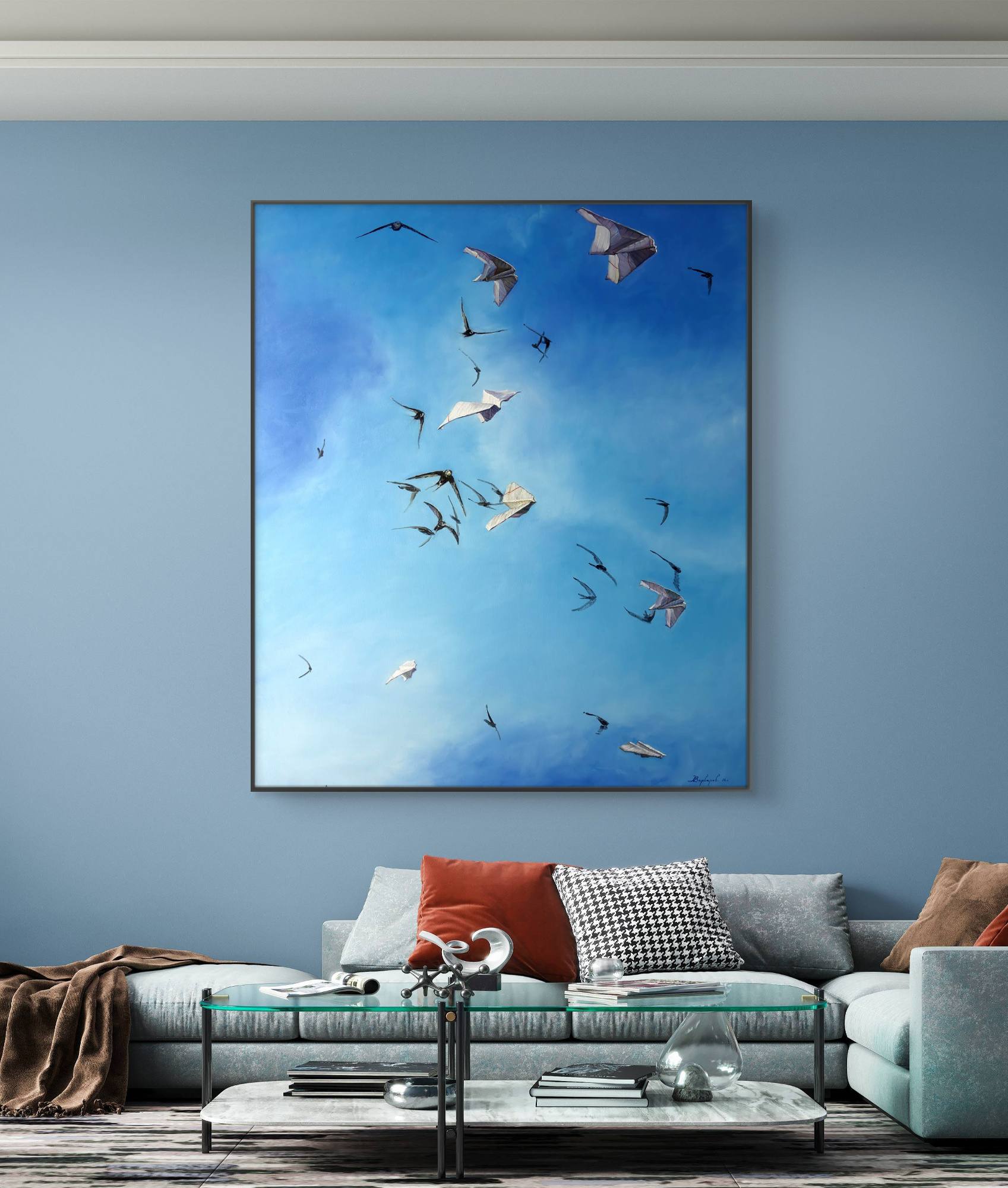 Framed artwork of birds flying in a blue sky above a living room with a sofa and coffee table.