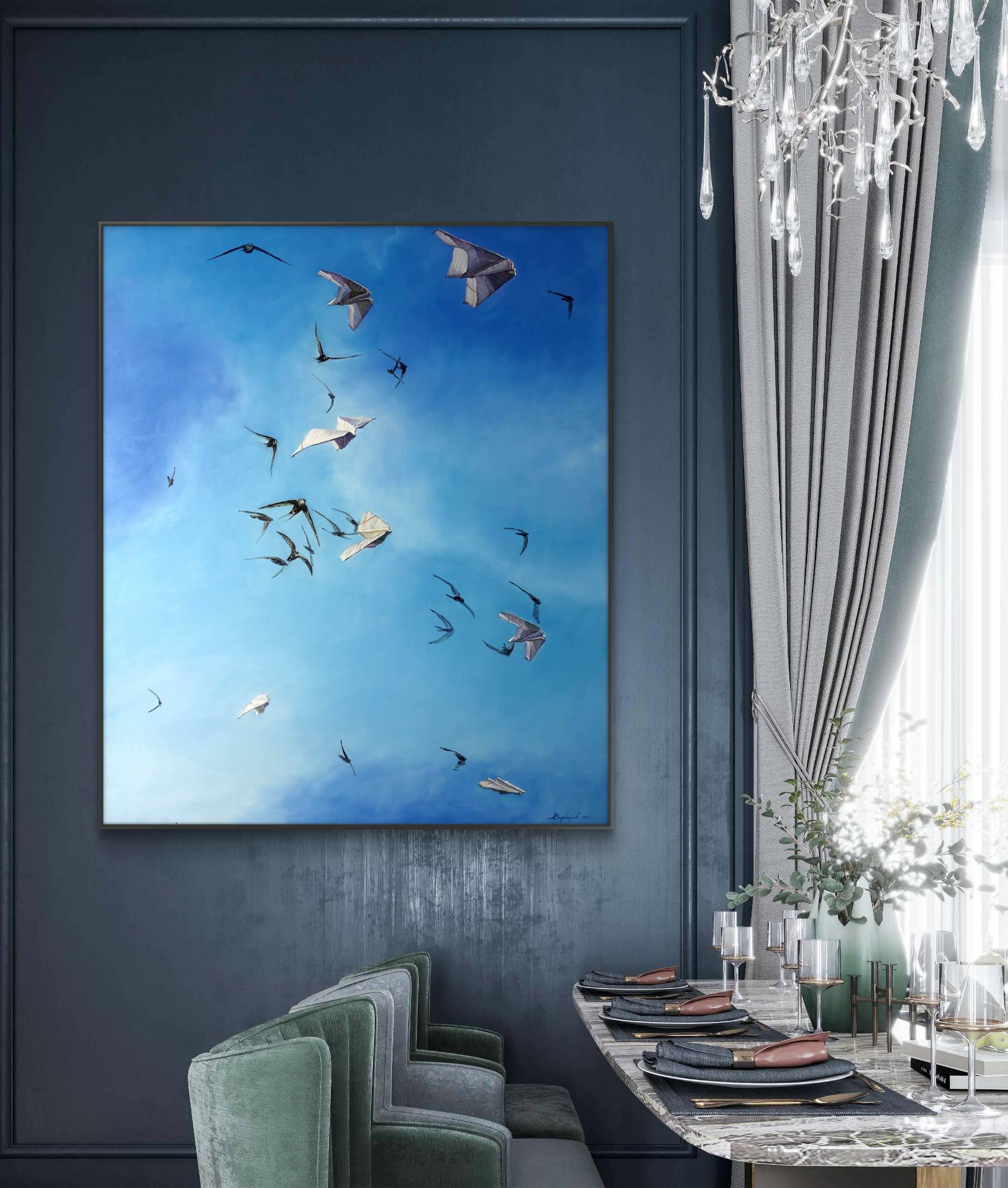 Framed artwork of birds flying in a blue sky above a dining area with green chairs and a chandelier.