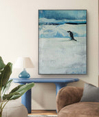 Framed artwork of a penguin on ice in a living room setting with a blue side table and brown sofa.