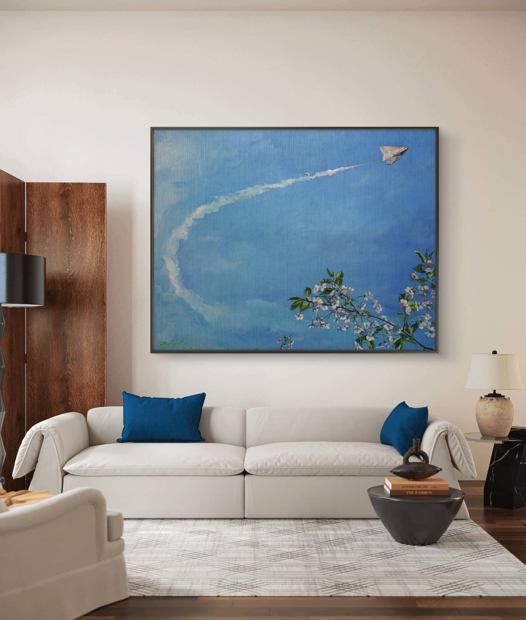 Living room with a white sofa, blue pillows, and a large framed artwork on the wall.