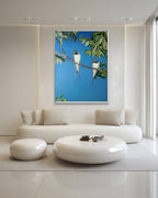 Modern living room with a white sofa, round ottoman, and a framed picture of birds on a branch.