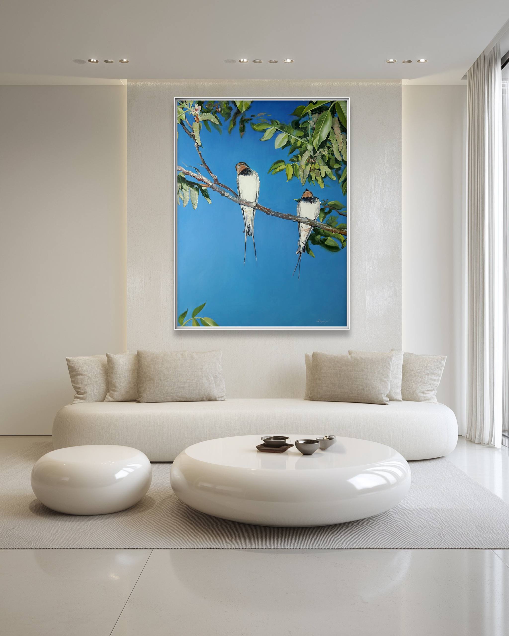 Modern living room with a white sofa, round ottoman, and a framed picture of birds on a branch.
