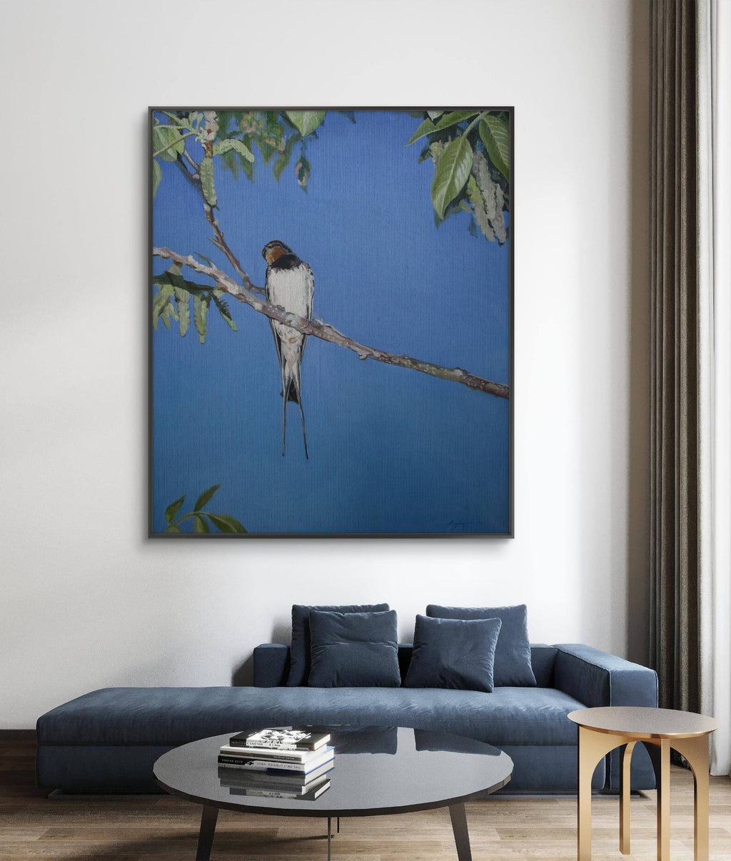 Framed artwork of a bird on a branch above a blue sofa in a living room.