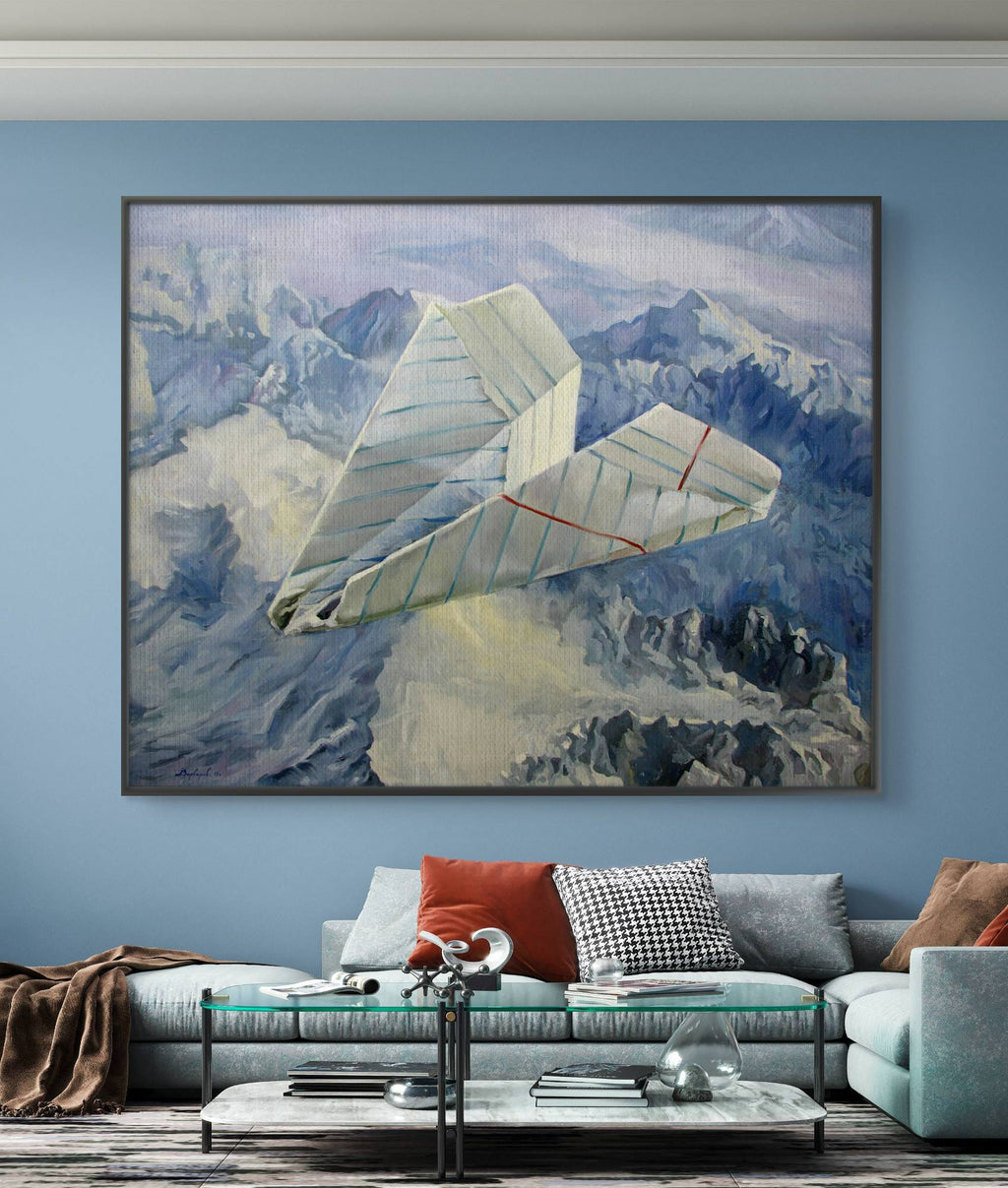 Bedroom with a large framed painting of a paper airplane over mountains, a white sofa with colorful cushions, and a coffee table.