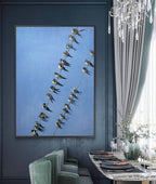 Framed artwork of birds on a branch against a blue wall in a stylish room with a chandelier and table setting.