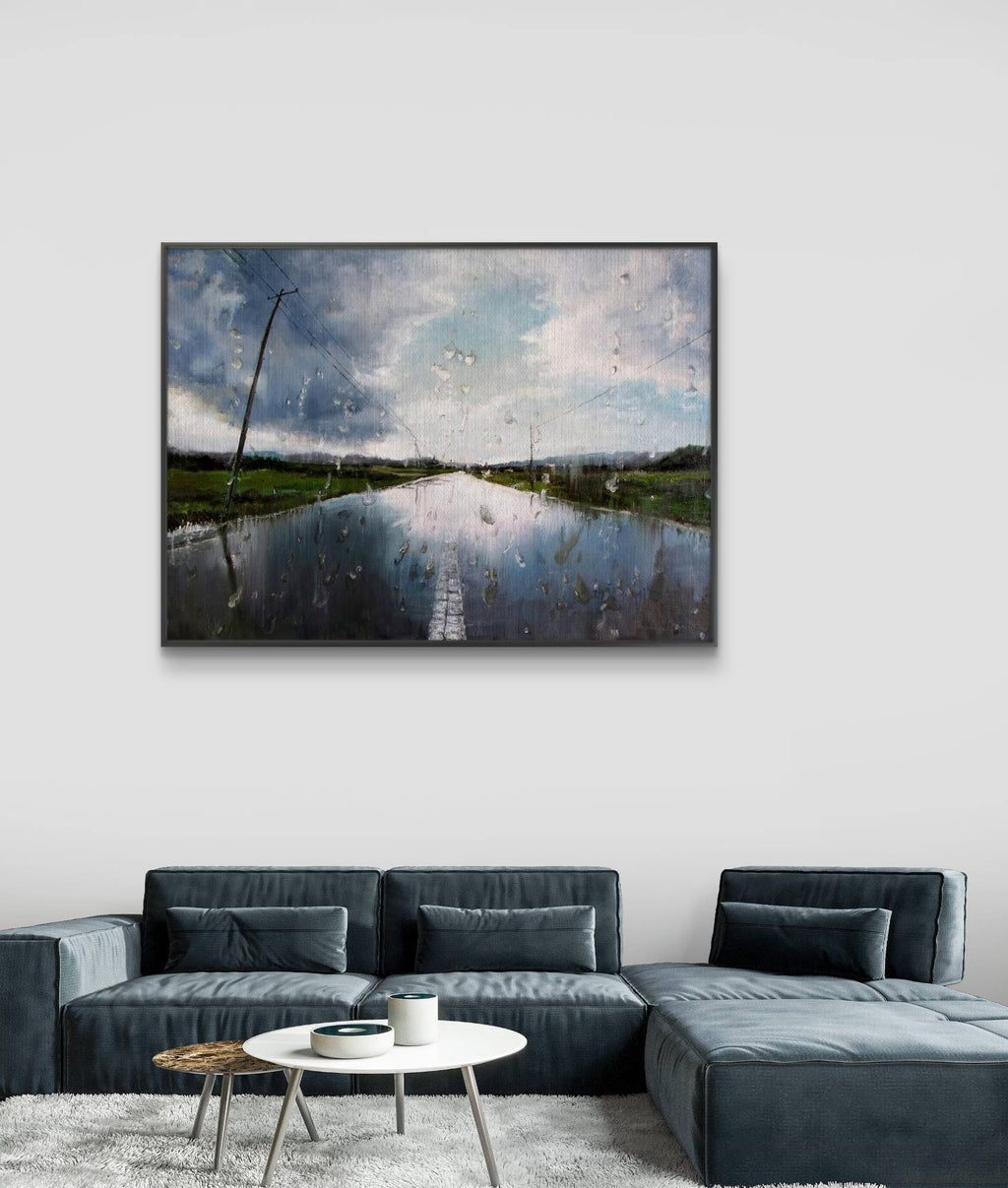 Framed artwork of a landscape with water and sky above a gray sofa.