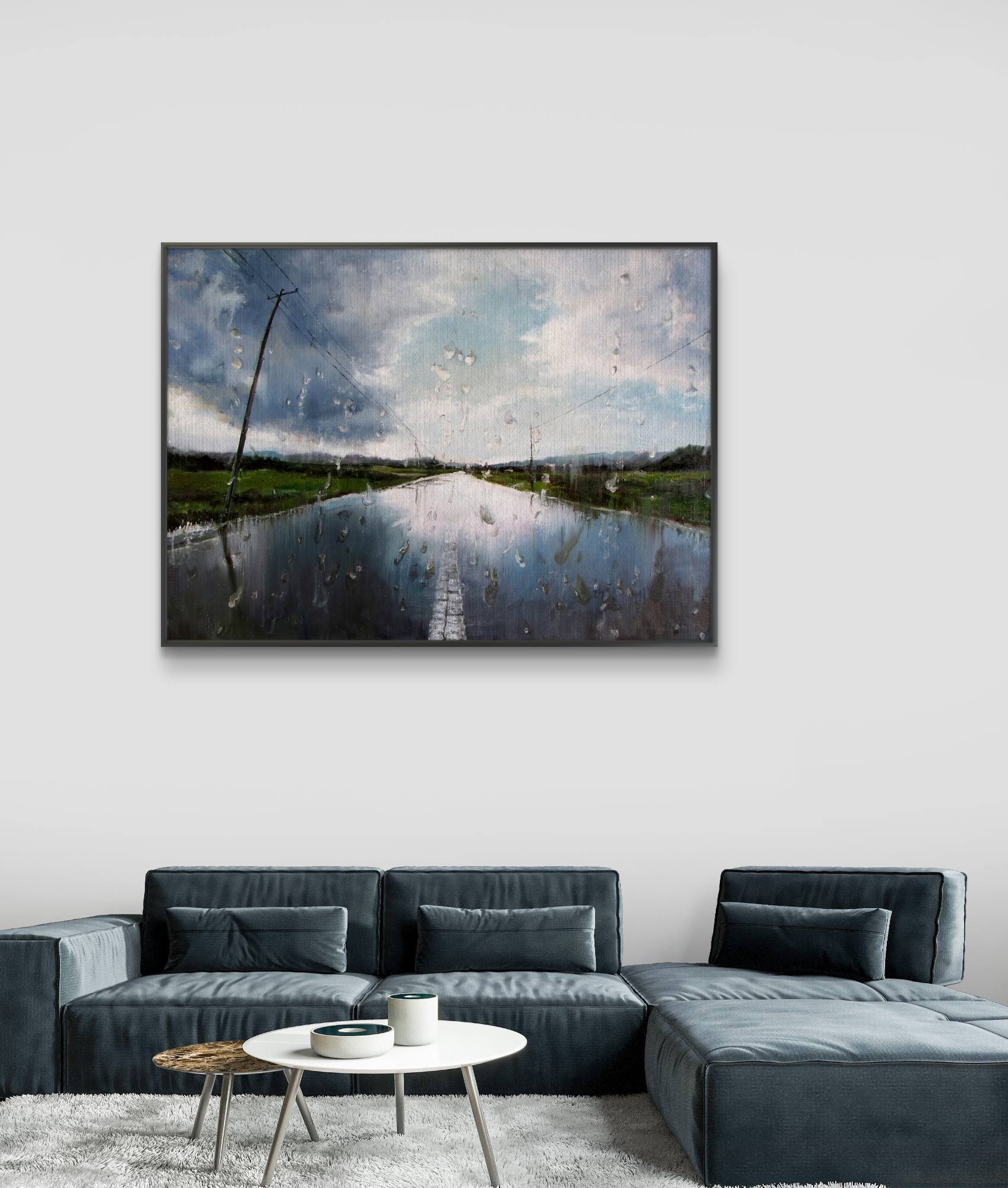 Framed artwork of a landscape with water and sky above a gray sofa.