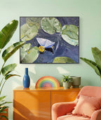 Living room with a painting of lily pads and a boat, a colorful rainbow decoration, and a blue vase on an orange cabinet.