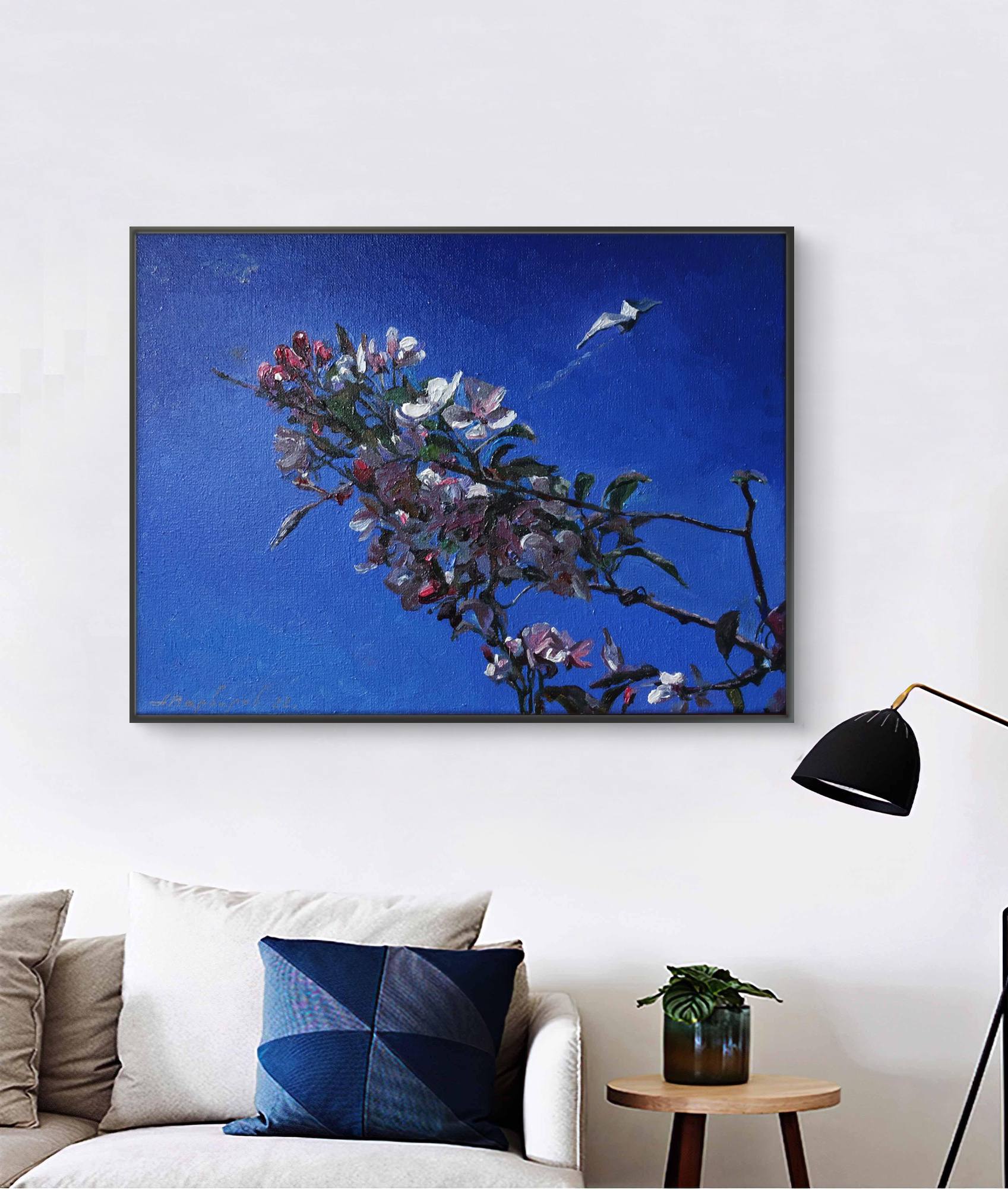 Framed artwork of a floral branch against a blue background in a living room setting.