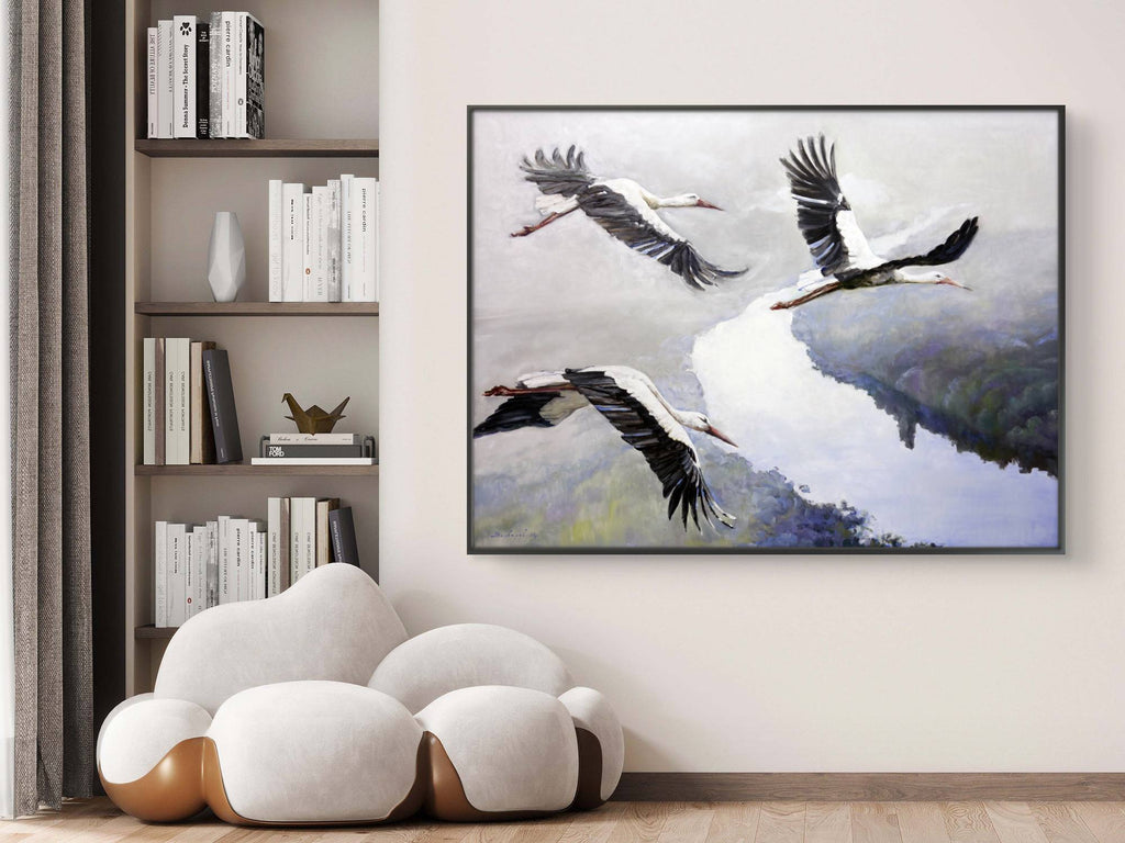 Framed artwork of birds flying over water in a room with a bookshelf and modern chair.