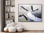 Framed artwork of birds flying over water in a room with a bookshelf and modern chair.