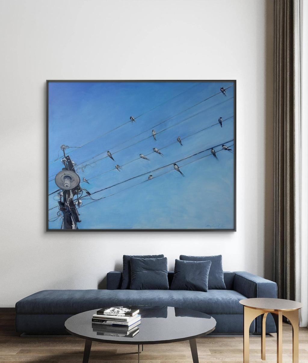 Framed artwork of power lines with birds on a blue sky background in a living room.