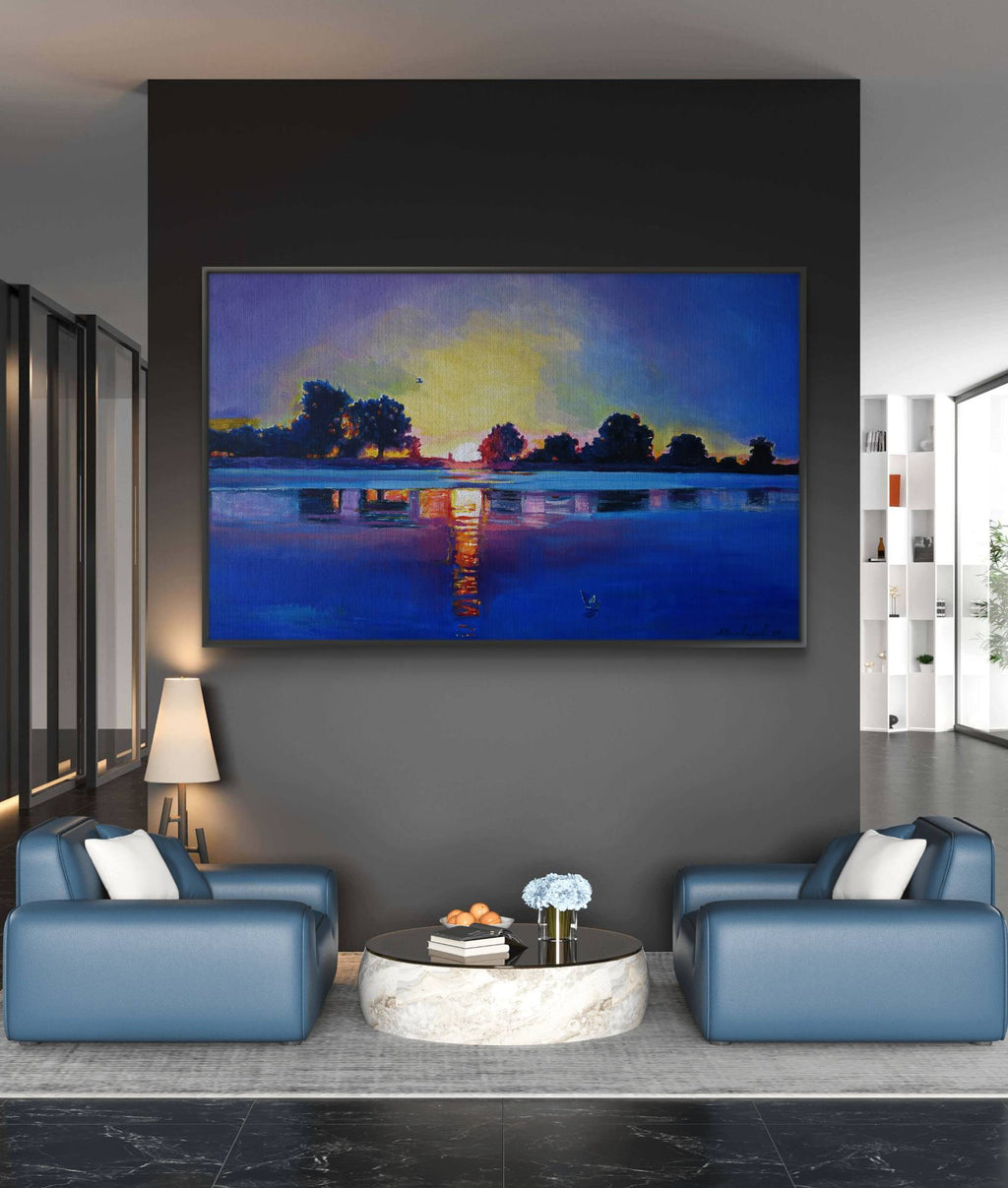 Modern living room with blue sofas and a large painting of a sunset over water.