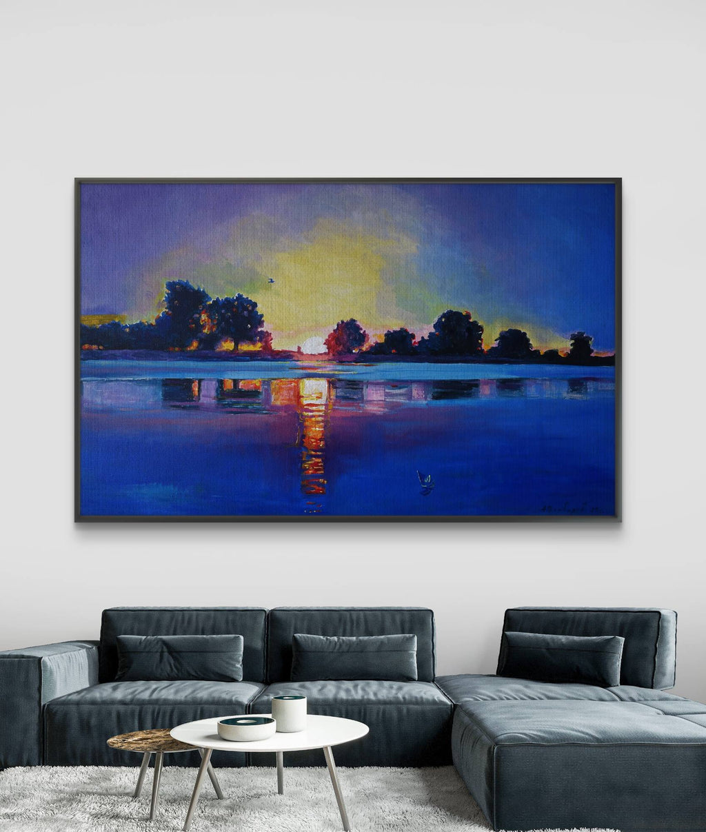 Framed artwork of a sunset over water on a wall above a sofa.