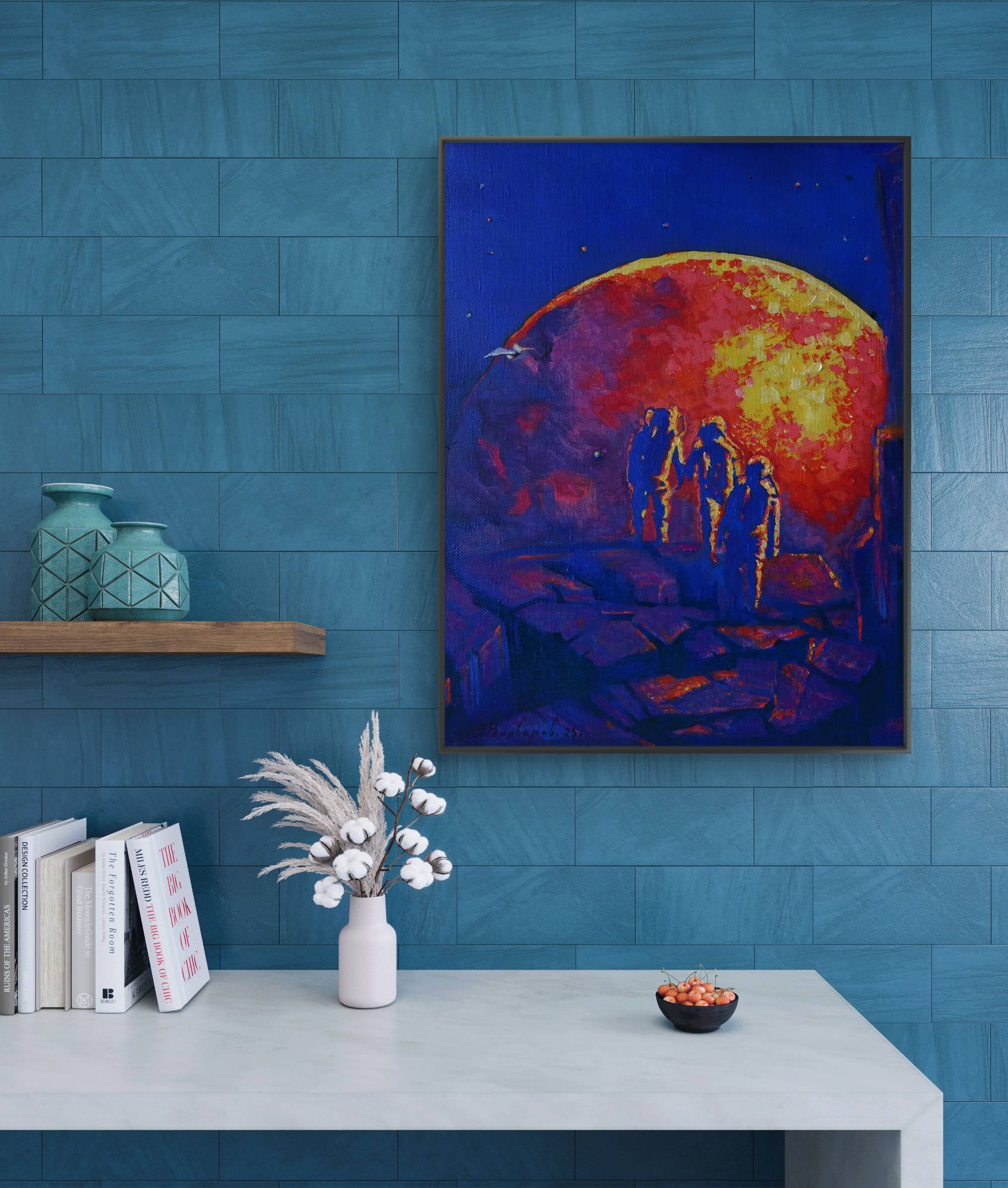 Framed artwork of a sunset over a mountain with silhouettes, displayed on a blue wall above a white table.
